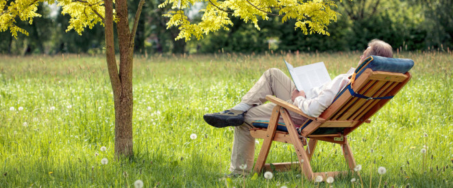 Man liegt im Liegestuhl und liest ein Buch im Garten