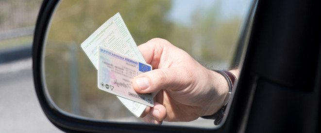 Hand im Rückspiegel zeigt Führerschein und Fahrzeugpapiere