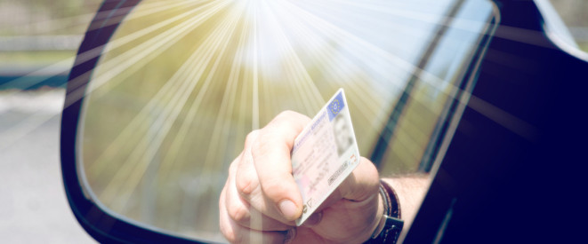 Nahaufnahme einer Hand, die den Führerschein aus dem Autofenster hält.