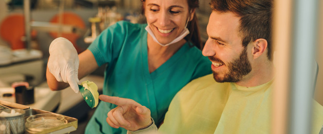 Zahnärztin und Patient schauen sich lachen einen Abdruck des Gebisses an