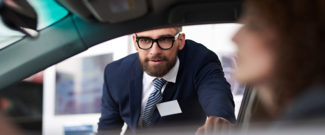 Experienced male sales manager demonstrating features of car when client sitting in vehicle