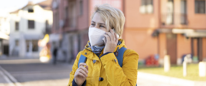 Frau in einen gelben Regenmantel, trägt eine FFP2 Maske