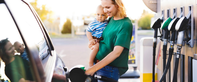 Junge Frau mit Baby auf dem Arm tankt glücklich ihr Auto