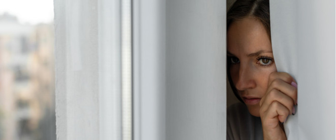 Frau schaut verängstigt hinter Gardine durchs Fenster Frau schaut verängstigt hinter Gardine durchs Fenster