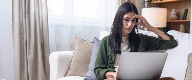Junge dunkelhaarige Frau sitzt konzentriert mit Laptop auf dem Sofa 
