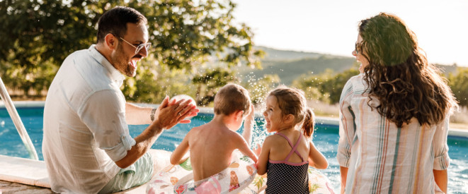 Familie mit zwei Kindern sitzt am Pool und lacht