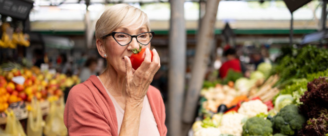 Ältere Frau auf dem Markt hält Tomate vors Gesicht