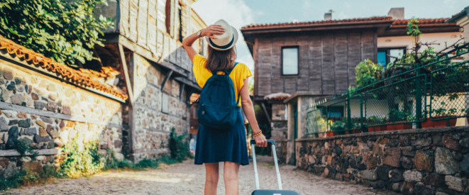 Frau in Sommerkleidung mit Rollkoffer im Urlaub