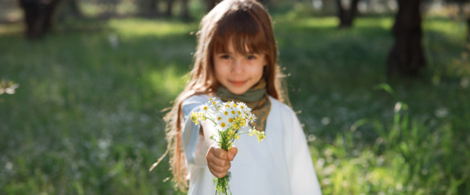 Mädchen steht bei Sonnenschein auf einer Wiese und hält einen Wildblumenstrauß in der Hand