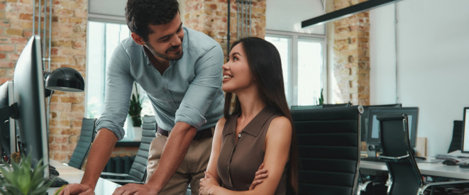 Happy to work with you! Two cheerful young colleagues in casual wear looking at each other with smile and discussing fresh ideas while working together in modern office. Workplace. Business concept.