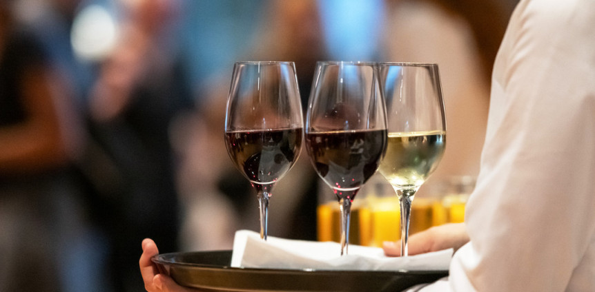 Kellner trägt ein Tablett mit zwei Rotwein- und einem Weißweinglas.