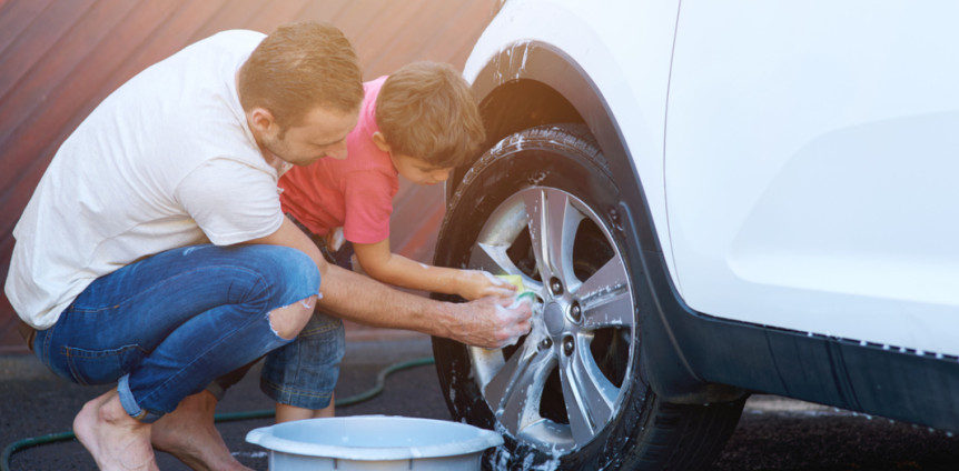 Mann und Kind waschen draußen vor der Garage ein Auto