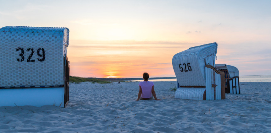 Eine Frau sitzt bei Sonnenuntergang zwischen zwei Strandkörben am Strand