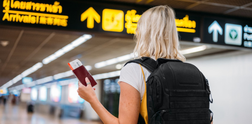 Frau mit Reisepass und Ticket in der Hand unter digitaler Anzeige am Flughafen