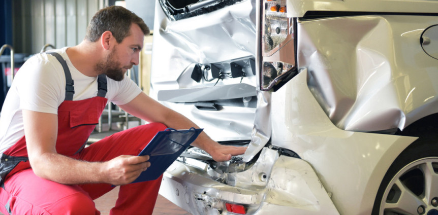 Mann KFZ-Mechaniker in rotem Overall prüft in Werkstatt Schaden an Auto