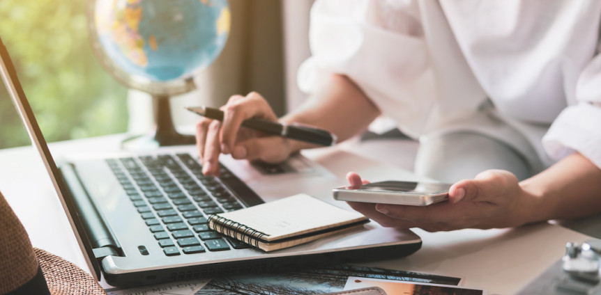 Person macht Urlaubsplanung mit Laptop, Smartphone und Notizblock