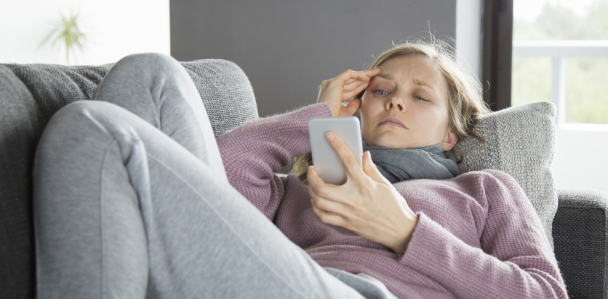 Kranke Frau mit Schal schreibt eine Nachricht am Handy.