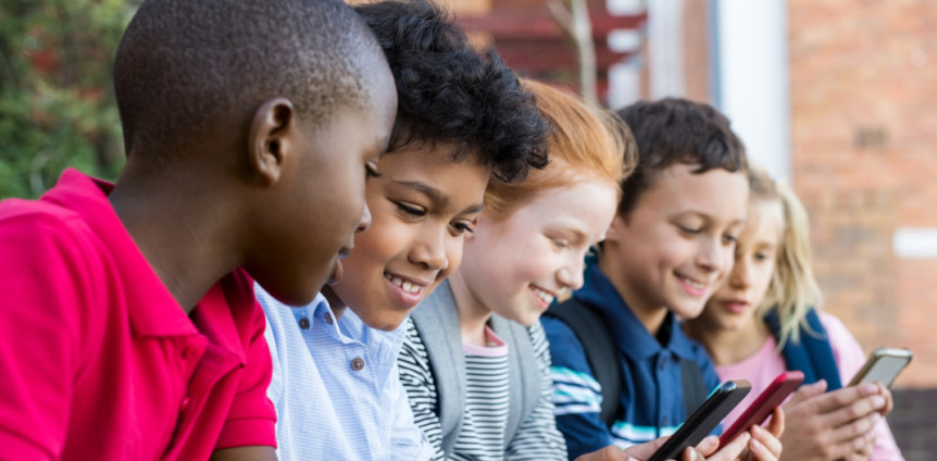 Fünf Schülerinnen und Schüler sitzen draußen und gucken auf Handys