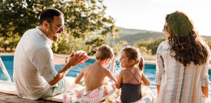 Familie mit zwei Kindern sitzt am Pool und lacht