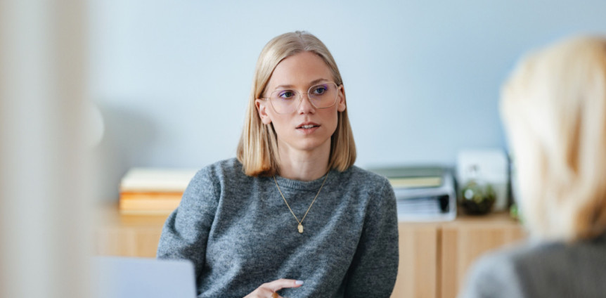 Junge blonde Frau sitzt bei einem Bewerbungsgespräch in einem Büro einer anderen Person gegenüber