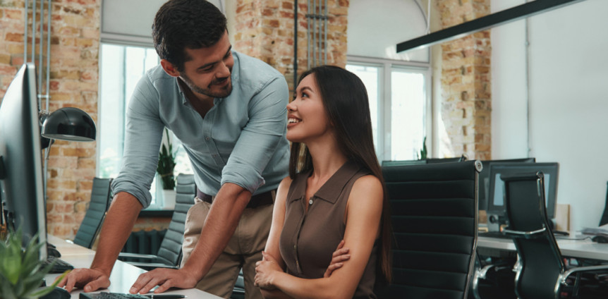 Happy to work with you! Two cheerful young colleagues in casual wear looking at each other with smile and discussing fresh ideas while working together in modern office. Workplace. Business concept.