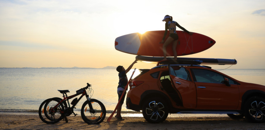 Silhouette couple traveler take paddle board to roof rack of car against sunset sky . Sport activity and lifestyle after workout at beach