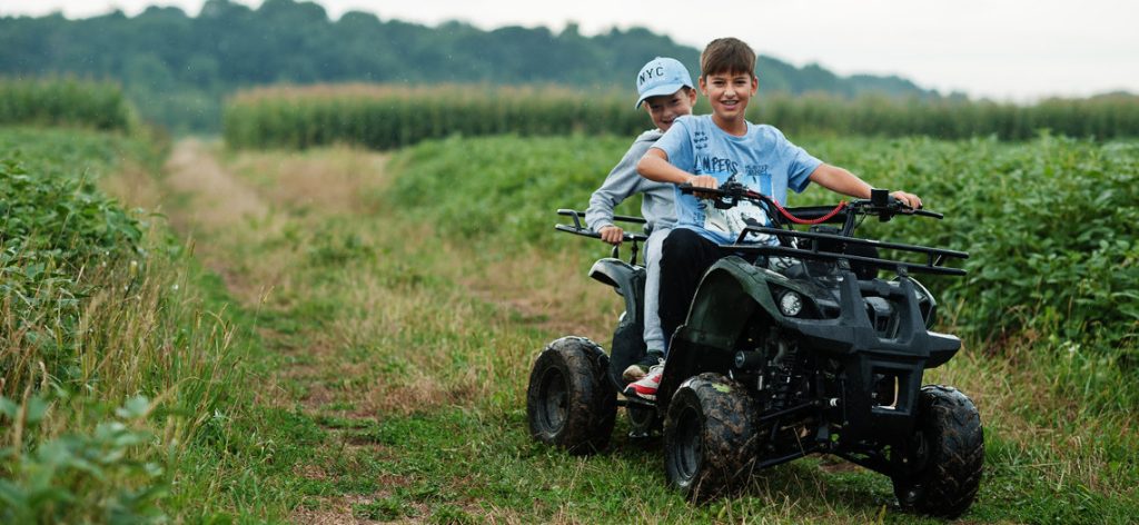 Zwei Jungs fahren gemeinsam auf eine Quad auf einem Feld.