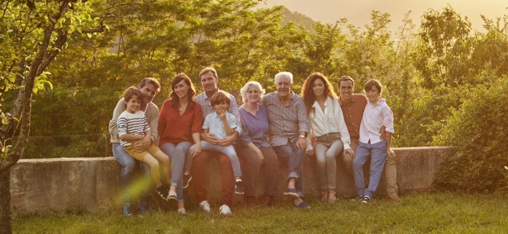 Mehrere Generationen einer Familie sitzen im Garten auf einer Mauer.