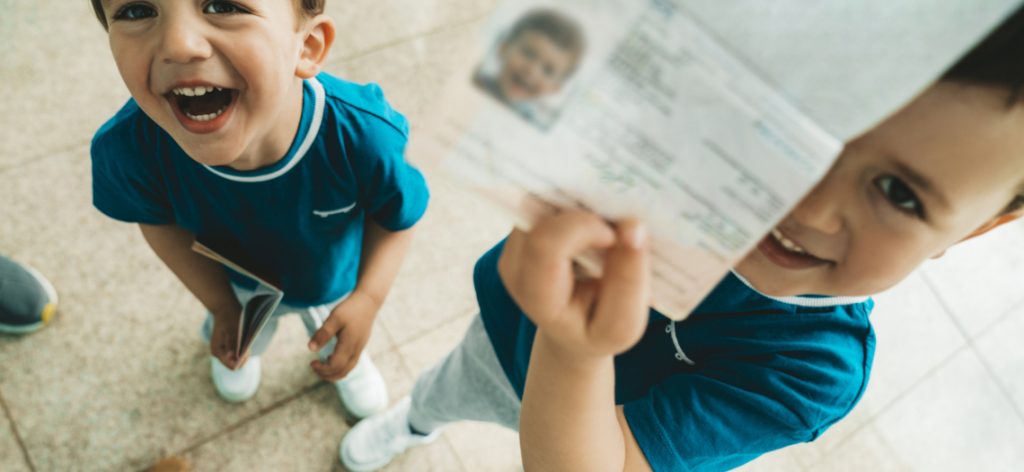 Zwei kleine Jungs lachen in die Kamera. Einer der beiden zeigt stolz seinen Reisepass.