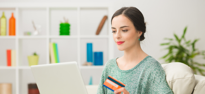 junge Frau mit Kreditkarte in der Hand sitzt vor dem Laptop