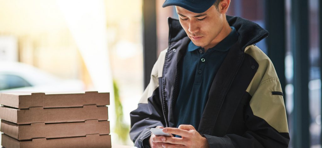 Junger Pizza-Bote schaut auf sein Handy