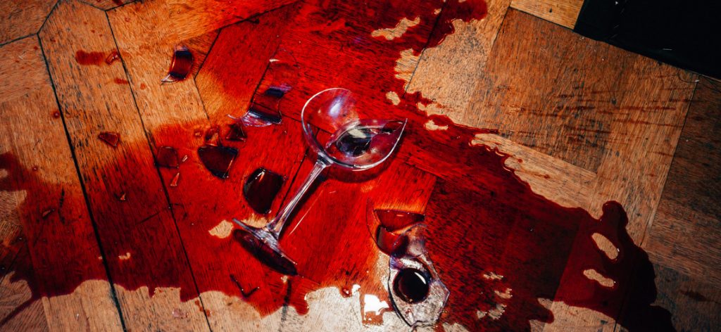 Wein aus umgeworfenem Weinglas fließt über den Parkettboden.