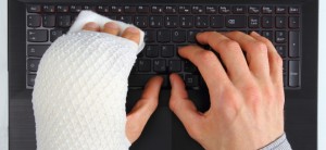 Zwei Hände auf einer schwarzen Computer-Tastatur. Die linke Hand ist eingegipst.