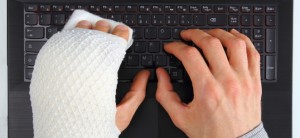 Krankmeldung: Rechte und Pflichten von Arbeitnehmern Zwei Hände auf einer schwarzen Computer-Tastatur. Die linke Hand ist eingegipst.