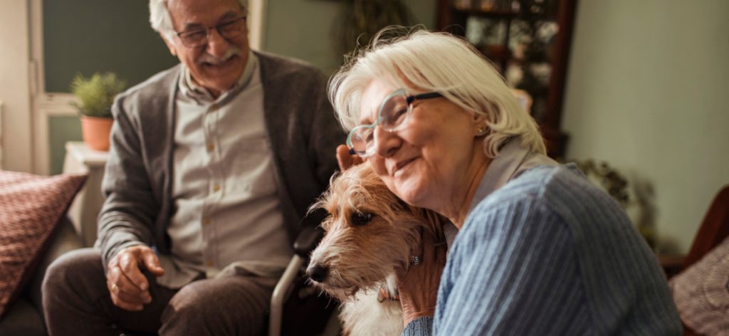 Älteres Paar mit Hund. Die Frau kuschelt mit ihrem Vierbeiner.