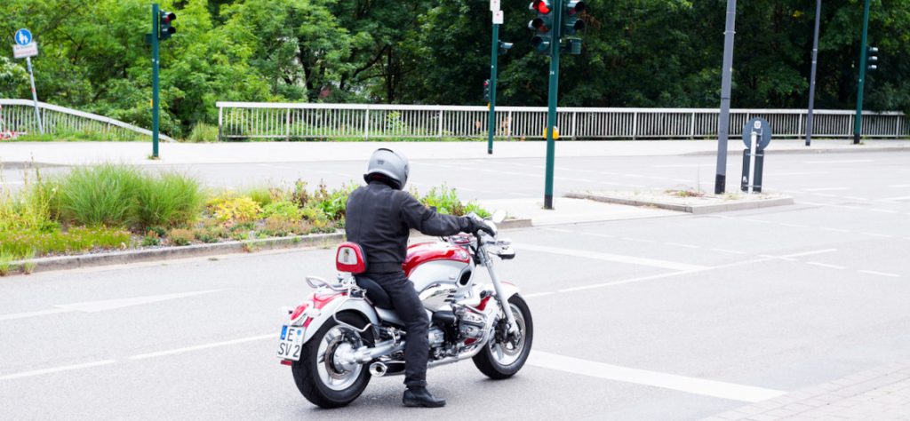Motorradfahrer wartet auf einer Kreuzung an einer roten Ampel.