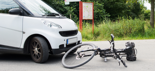 Fahrradunfall: Unachtsamer Radfahrer trägt Alleinschuld. Neben einem weißen Smart liegt ein Rad auf dem Asphalt.