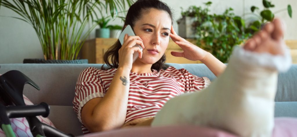 Frau mit Gipsbein telefoniert mit dem Handy.