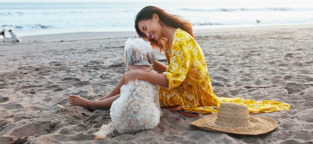 Frau sitzt mit ihrem Hund am Strand und lacht