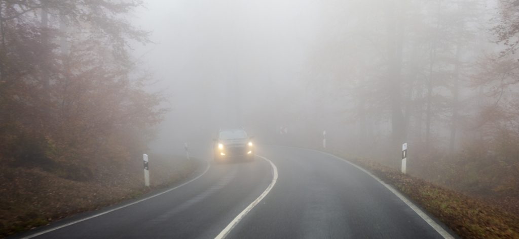 Auto fährt mit eingeschalteten Scheinwerfern über eine nebelverhangene Straße