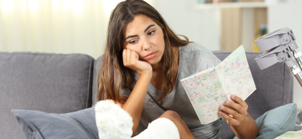 Frau sitzt traurig mit Stadtplan auf Sofa. Neben ihr liegen Krücken.