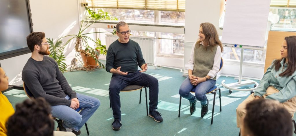 Patientinnen und Patienten sitzen mit ihrem Psychotherapeuten bei der Gruppentherapie in einem Stuhlkreis