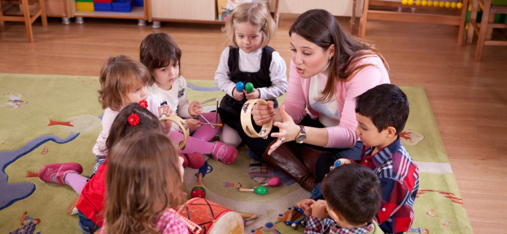 Frau musiziert mit kleinen Kindern in einem Sitzkreis.