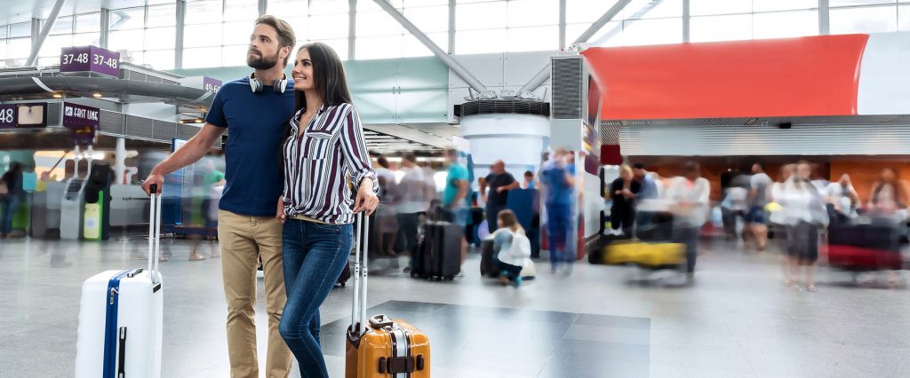 Paar steht aneinander gelehnt mit den Koffern am Flughafen.