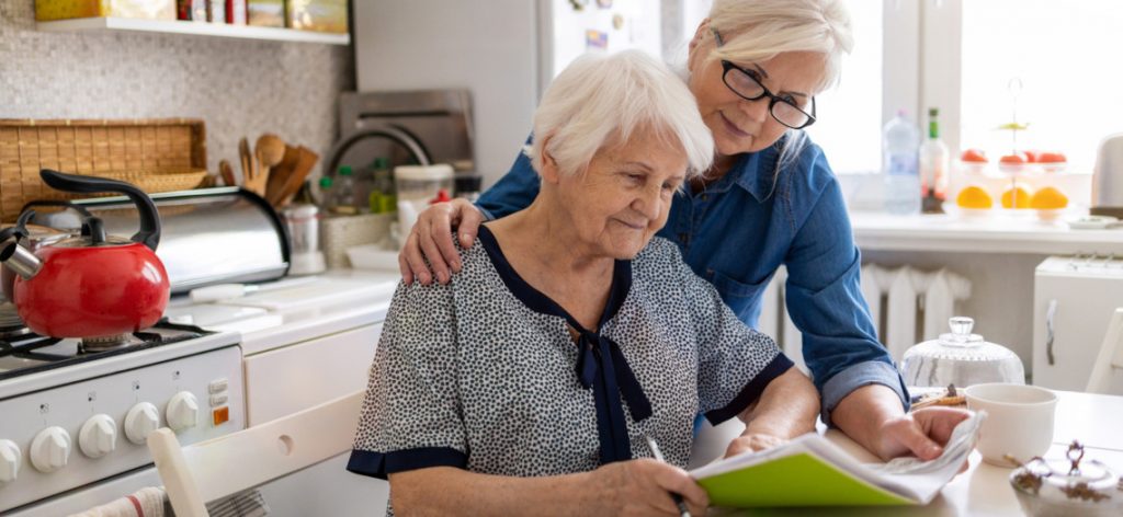 Betreuerin und ältere Frau lesen gemeinsam in einem Notizbuch in der Küche.