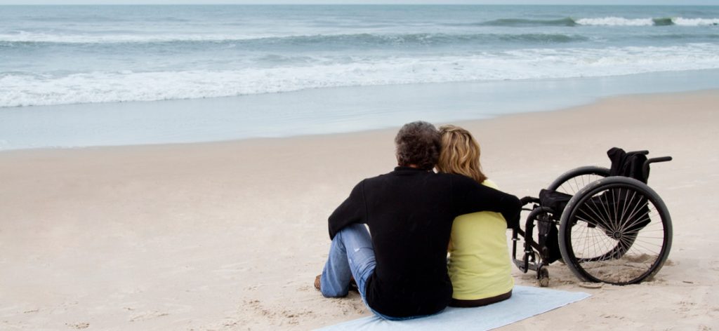 Paar sitz umschlungen am Strand und schaut aufs Meer.