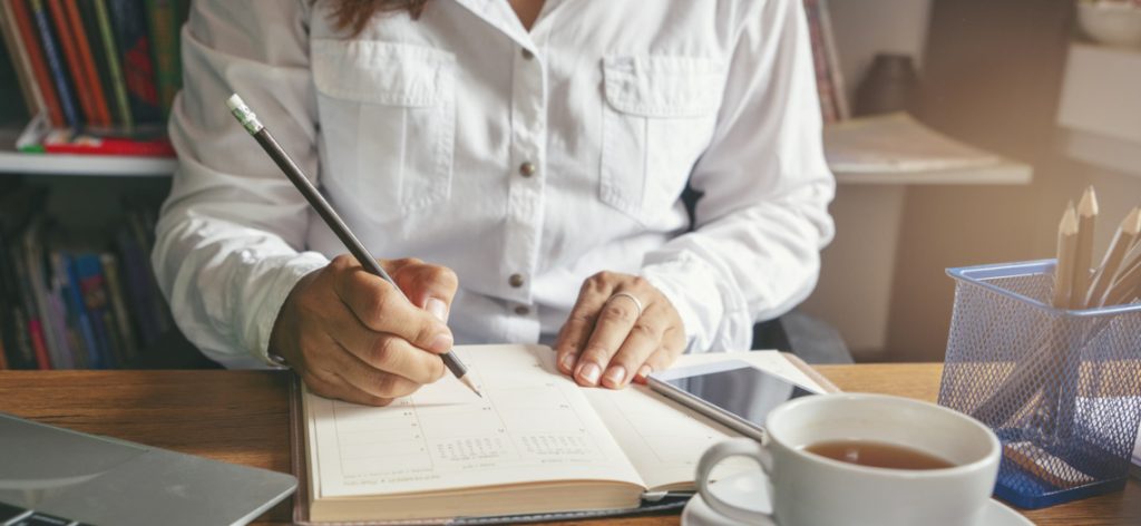 Frau schreibt in einen Buchkalender.