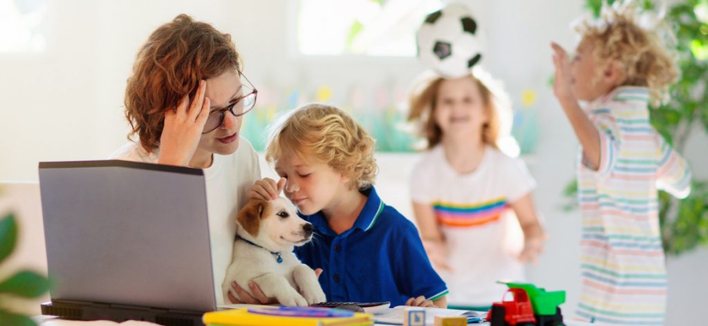 Eine Mutter sitzt am Laptop, während Kinder um sie herum spielen und sieht verzweifelt aus