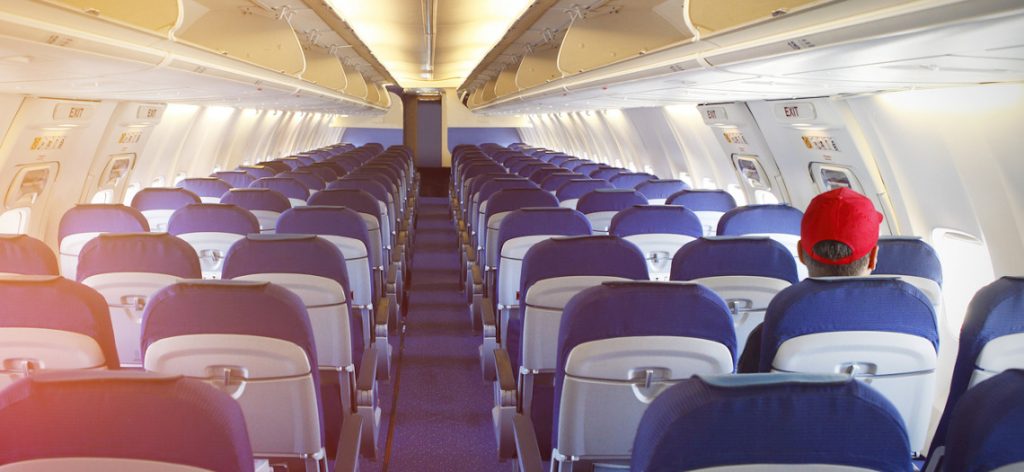 Reisewarnung wegen Corona: Bedeutung und Folgen für Urlauber Mann mit roter Kappe sitzt in einem leeren Flugzeug.