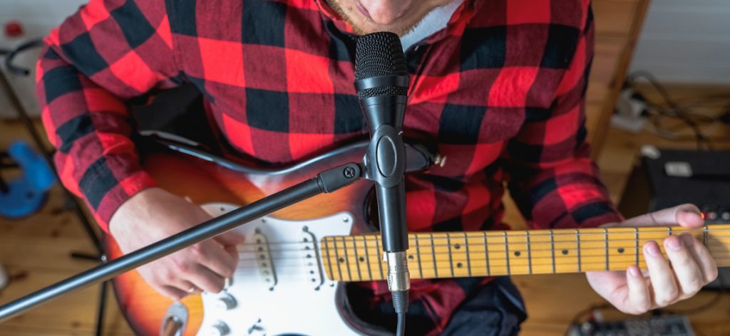 Ein Mann sitzt mit einer Gitarre sitzt vor einem Mikrofon. 